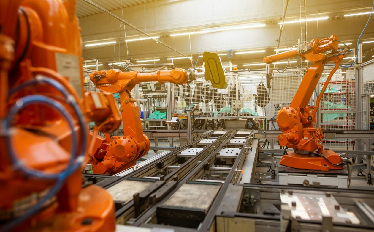 Braços robóticos laranjas em linha de produção industrial automatizada