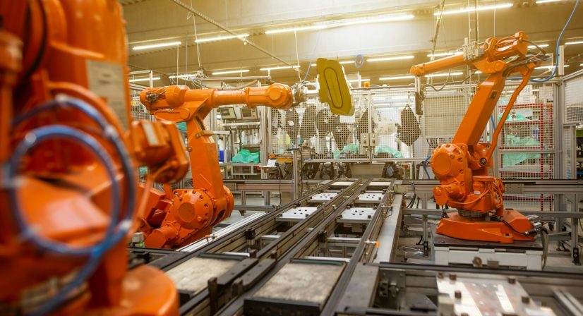 Braços robóticos laranjas em linha de produção industrial automatizada